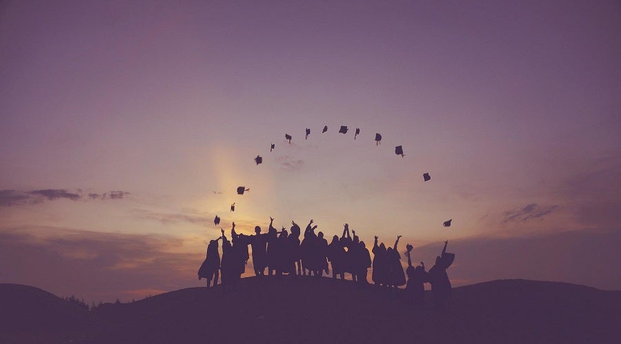 graduates standing on a hill at dawn and throwing their caps in the air
